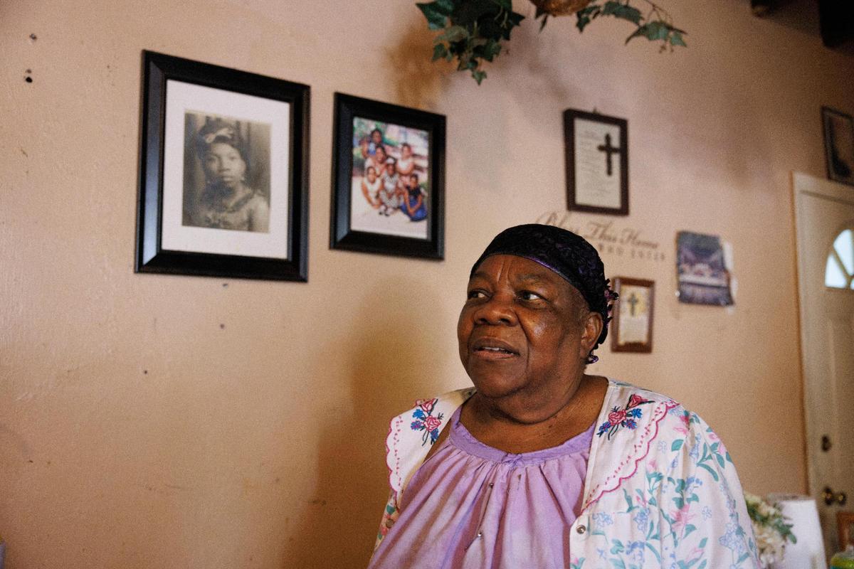 Mimose Martial poses in front of a photo of herself at 20 years old and other family photos inside her Miami home.