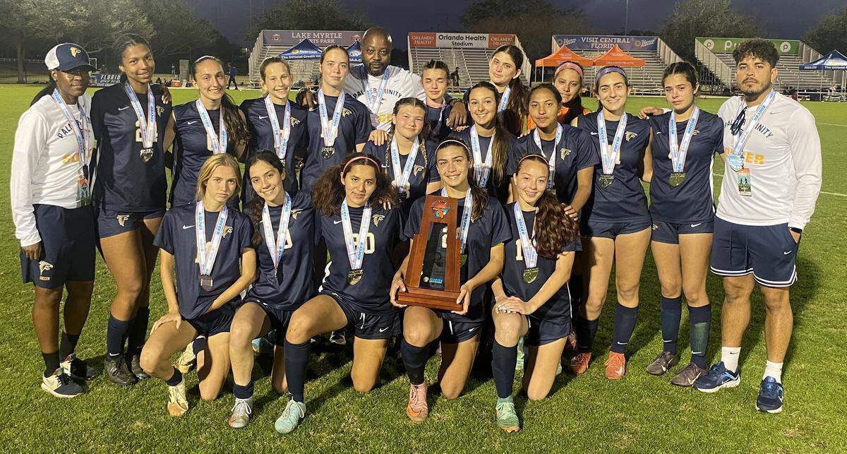 The Palmer Trinty players and coaches gather around the Class 2A girls soccer state runners-up trophy on Wednsesday at Lake Myrtle Sports Complex in Auburndale.