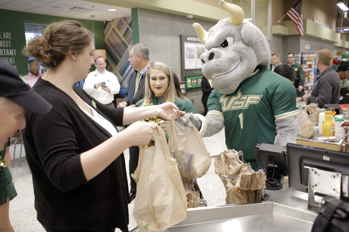 (From left) Jessica Dwyer, a Publix customer service team leader assists USF Bulls cheerleader Haley Ayrsman, 20, and USF mascot ‘Rocky the Bull’ during the grand opening of the Publix on USF’s campus in Tampa. On Thursday, Dec. 6, 2018, Publix opened its first supermarket on a main college campus at the University of South Florida in Tampa.
