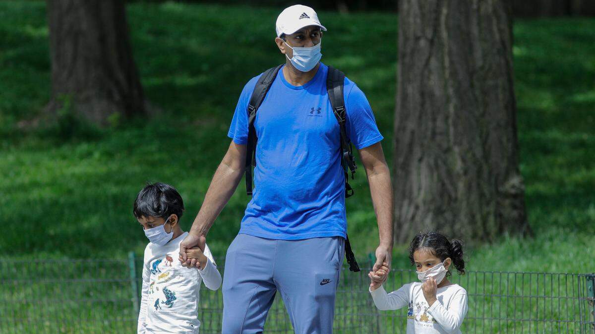 In this stock photo is a man wearing a protective mask helps children cross a running path in Central Park Saturday, May 16, 2020, in New York.