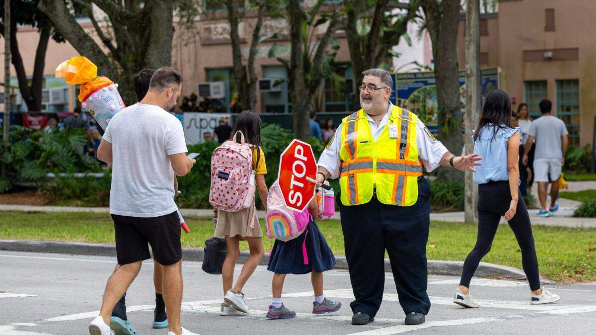 El guardia de cruce escolar Danny Arocha ayuda a padres y niños a cruzar la calle el primer día de clases en la primaria Sunset en South Miami, Florida, el jueves 17 de agosto de 2023. 