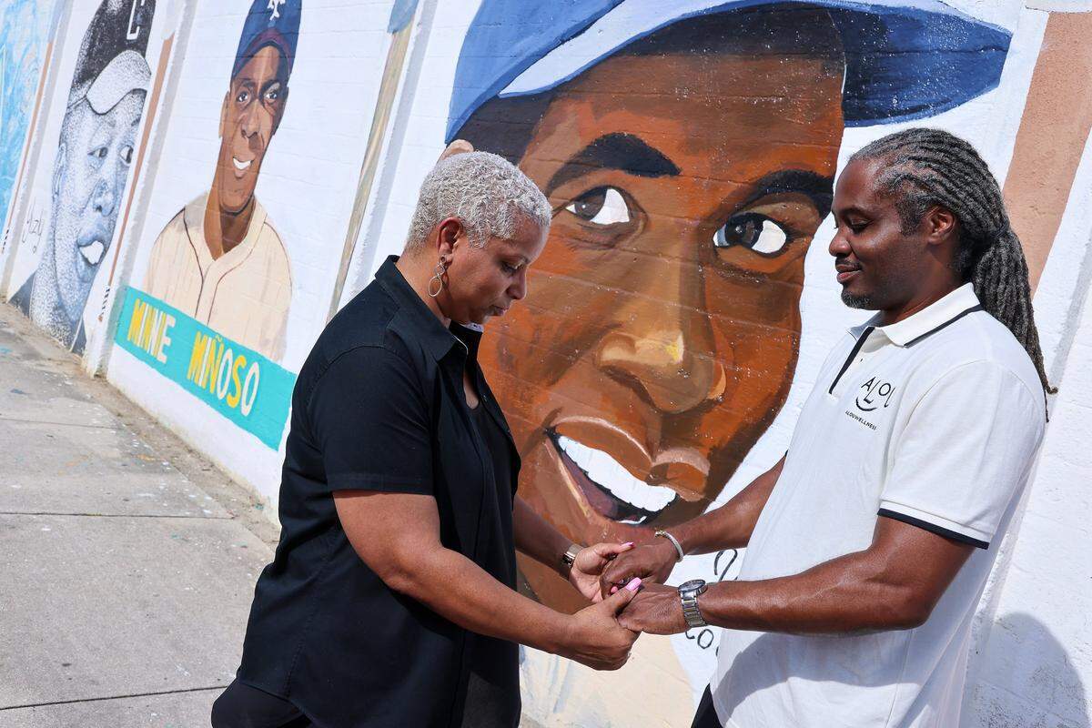 Saliha Nelson of URGENT, Inc. left, and Alex Douyon, hold hands in meditation in front of the restored murals shortly after the press conference regarding the Historic Dorsey Park Restoration & Renewal project on Wednesday, August 20, 2025, in Miami, Florida.