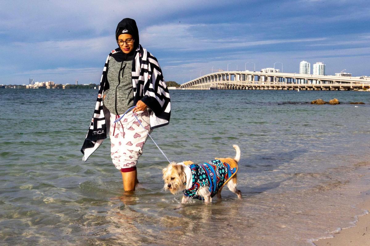 A bundled up Kristal Garcia, 48, walks her dog Jay in the water at Hobie Island Beach Park in Key Biscayne, Florida, on Saturday, Dec. 24, 2022.