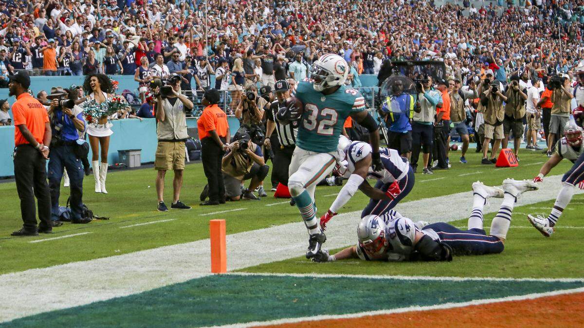 Miami Dolphins running back Kenyan Drake #32 runs for the winning touchdown past the defense of New England Patriots tight end Rob Gronkowski #87 and defensive end J.C. Jackson #27 during fourth quarter of an NFL football game against the New England Patriots at Hard Rock Stadium on Sunday, December 9 2018, in Miami Gardens. Dolphins won 34-33.