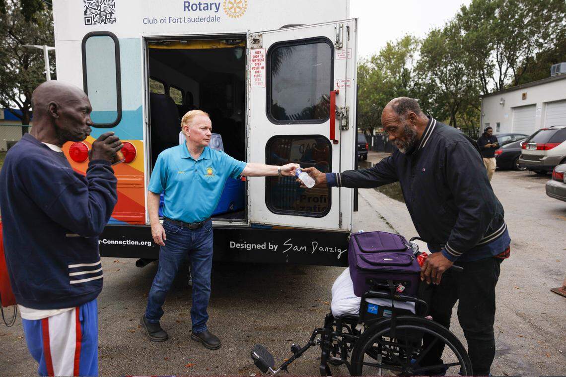 Garry Smyth, en el centro, cofundador y director ejecutivo, reparte bebidas desde la parte trasera del autobús que maneja Rotary Connection, una iniciativa sin fines de lucro que ofrece transporte gratuito a servicios sociales en la ciudad, mientras Alex Wright, a la izquierda, espera el autobús en LifeNet4Families el lunes 12 de enero de 2026, en Fort Lauderdale, Fla. 