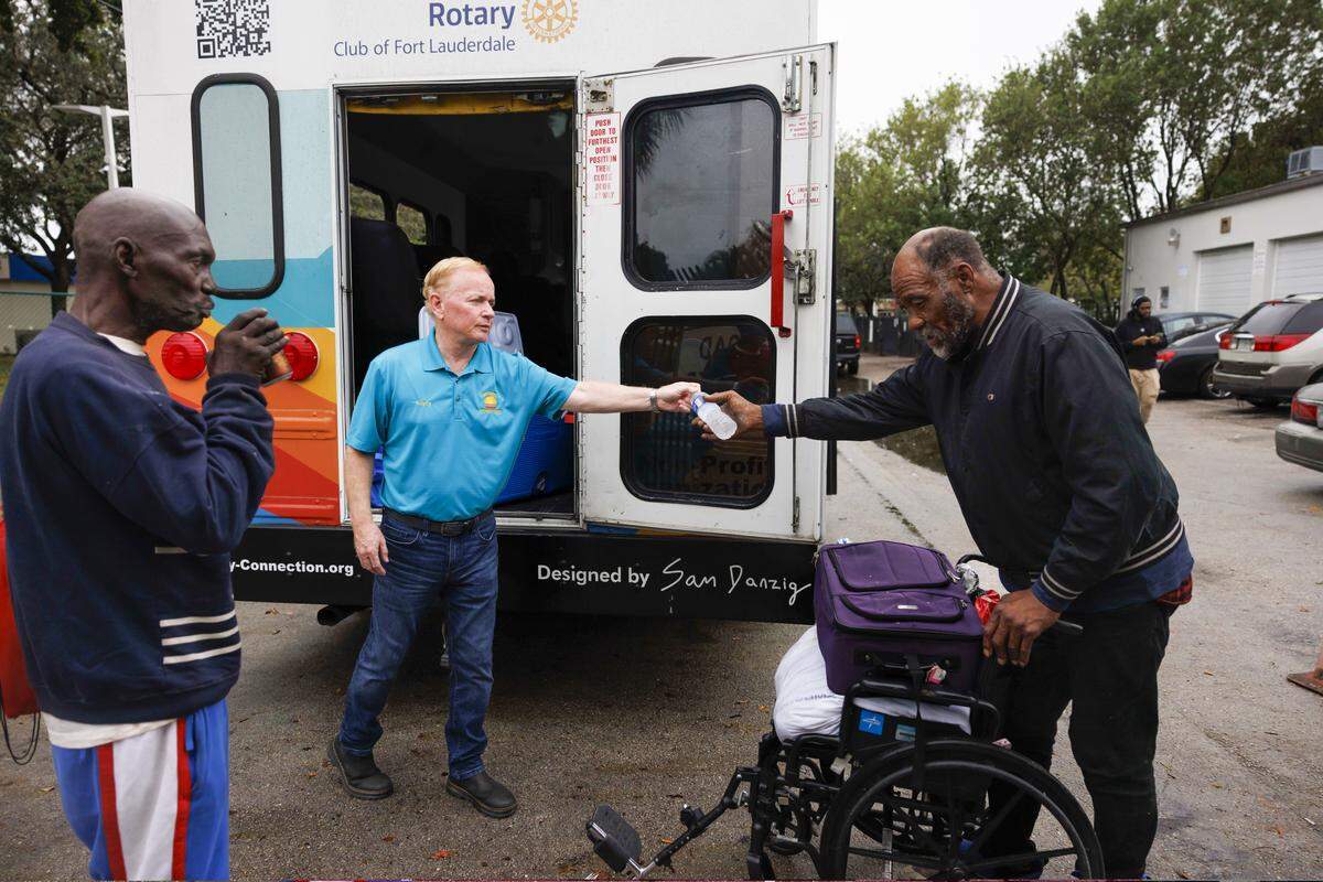 Garry Smyth, center, co-founder and executive director, hands out drinks out of the back of the bus run by Rotary Connection, a nonprofit initiative that offers free bus transportation to social services around the city, while Alex Wright, left, hangs out waiting for the bus at LifeNet4Families on Monday, Jan. 12, 2026, in Fort Lauderdale, Fla. 
