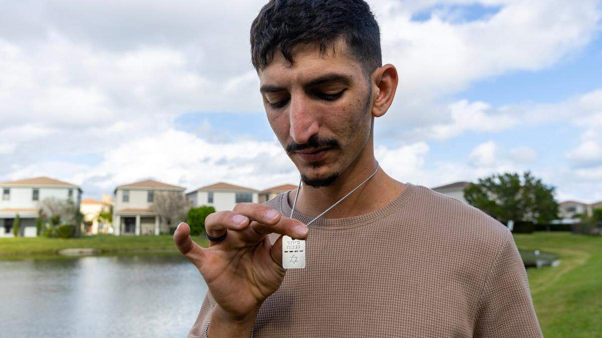 Survivor Roi Joseph Benaim, 26, holds a pendant that reads ‘Bring Them Home - Now’ as he stands outside his uncle’s home inside Aventura Isles in Aventura, Florida, on Thursday, January 4, 2024. Benaim was with his brother and friends when Hamas terrorists attacked an Israeli music festival near the Gaza Strip.