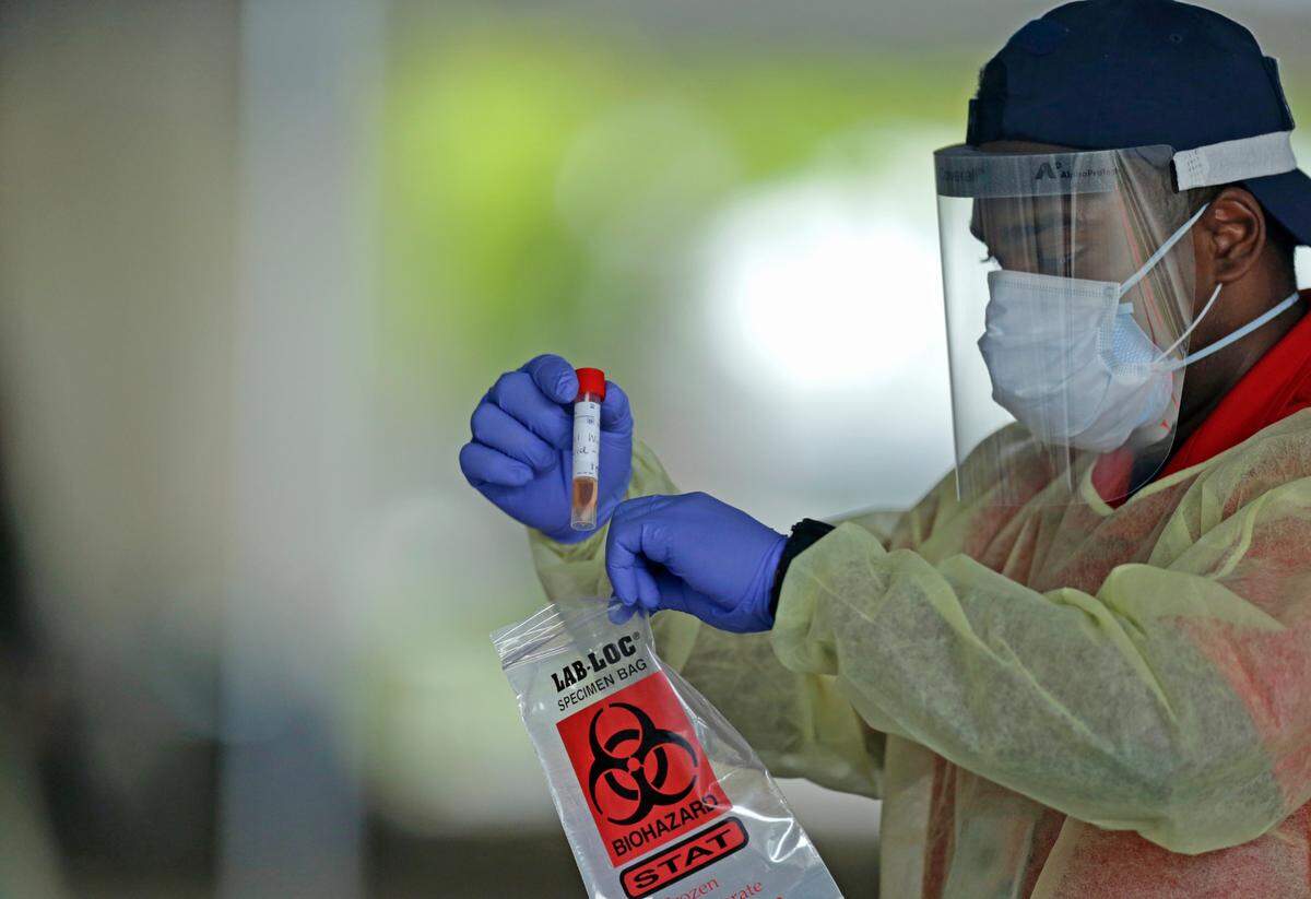 An American Medical Response health worker holds a swab test from a citizen after a test at the COVID-19 drive-thru testing center at Holiday Park, 1150 G. Harold Martin Drive in Fort Lauderdale, on Thursday, April 30, 2020.