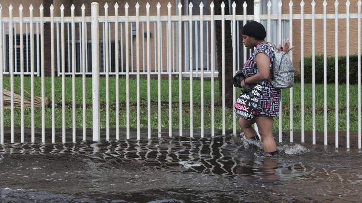 A woman uses the fence to support herself as she walks through high flood waters in Palm Spring North in North Miami-Dade County.