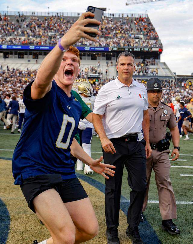 A Georgia Tech football fan takes a selfie in front of Miami Hurricanes head coach Mario Cristobal as the Yellow Jackets celebrate the defeat of the Canes in an NCAA game at Bobby Dodd Stadium at Hyundai Field in Atlanta, Georgia on Saturday, November 9, 2024. This image was one of the photos that was part of the package that won first place in the Florida Society of News Editors Sports photography category.