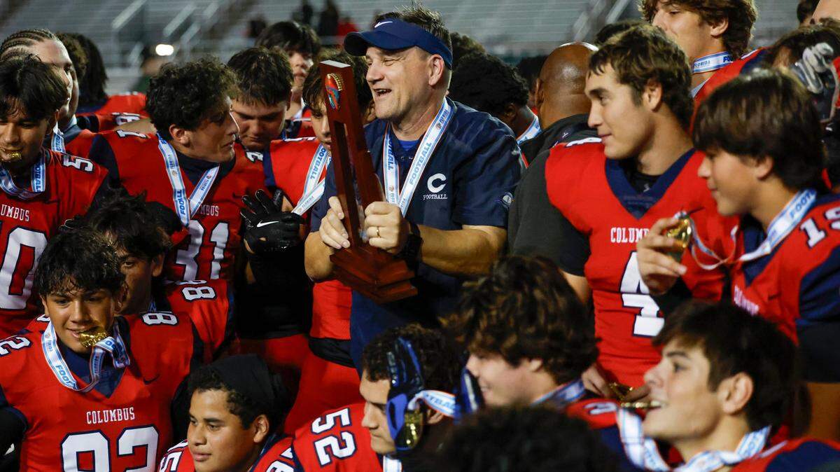 Columbus Explorers head coach Dave Dunn holds the championship trophy as the team celebrates defeating the Mandarin Mustangs in the FHSAA State Championships, Class 4M, at Bragg Memorial Stadium in Tallahassee, Florida, on Friday, December 8, 2023.