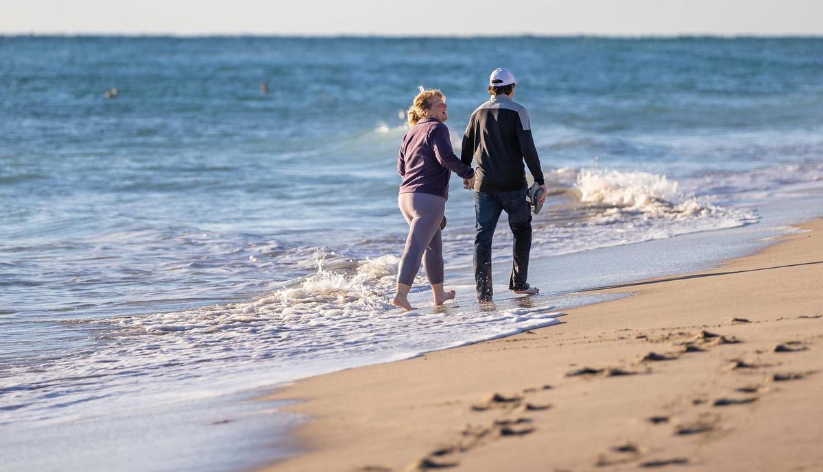Natalie Suiter and Jason Rayburn walk near the shoreline as temperatures dip into the mid 40s on Saturday, Jan. 14, 2023, in Hollywood, Fla.