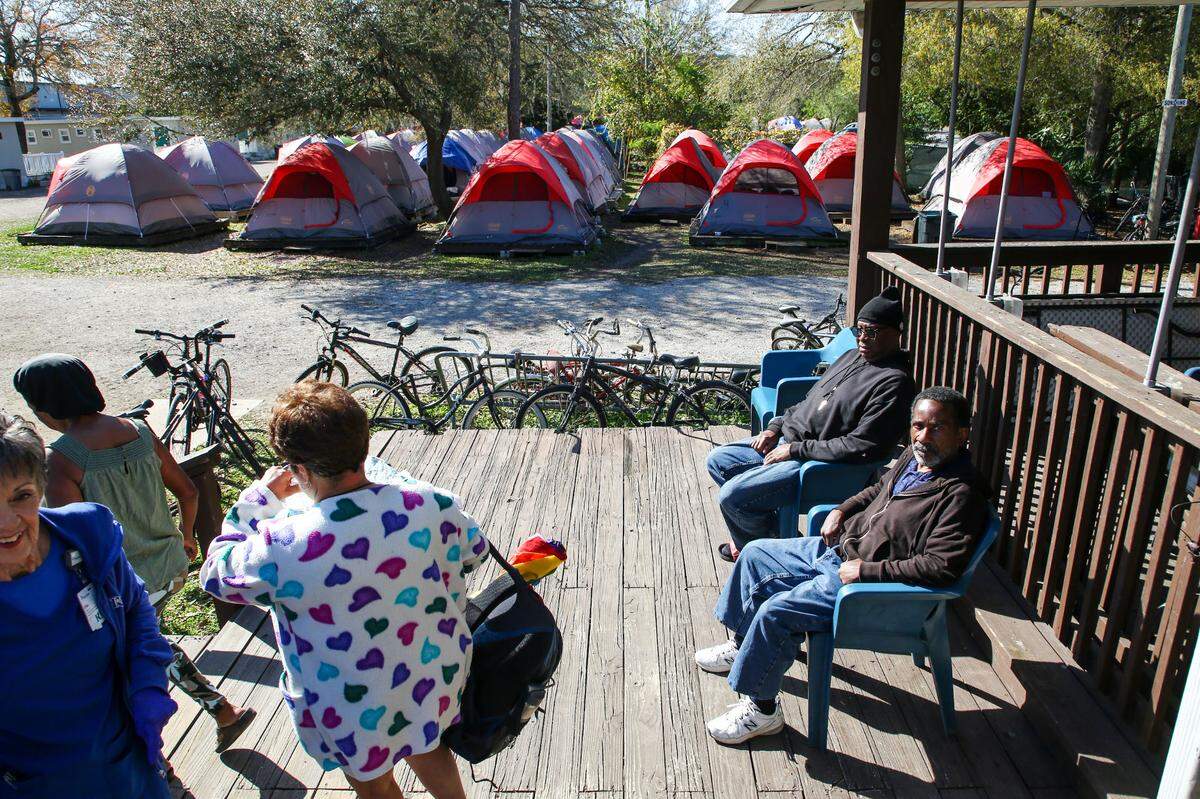 Pinellas Hope residents Darryl McCullough, center, right, and Anthony Hayes, right, soak up some morning sun at the community shelter on Tuesday, Feb 27, 2024, in Clearwater. Residents live in the 134 tents, background, and 90 cottages available in the community.