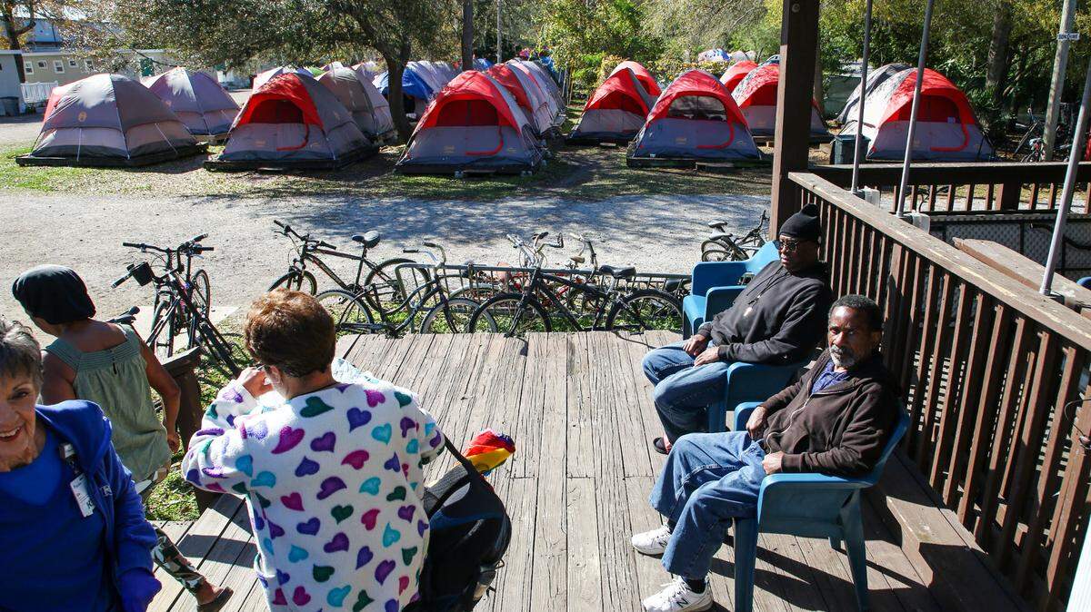 Pinellas Hope residents Darryl McCullough, center, right, and Anthony Hayes, right, soak up some morning sun at the community shelter on Tuesday, Feb 27, 2024, in Clearwater. Residents live in the 134 tents, background, and 90 cottages available in the community.