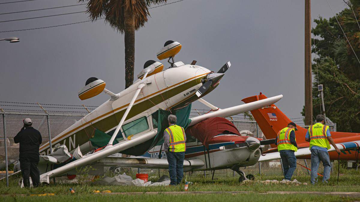 Airport workers look at an airplane that flipped over due to winds produced by Hurricane Ian at North Perry Airport in Pembroke Pines, Florida on Wednesday, September 28, 2022.