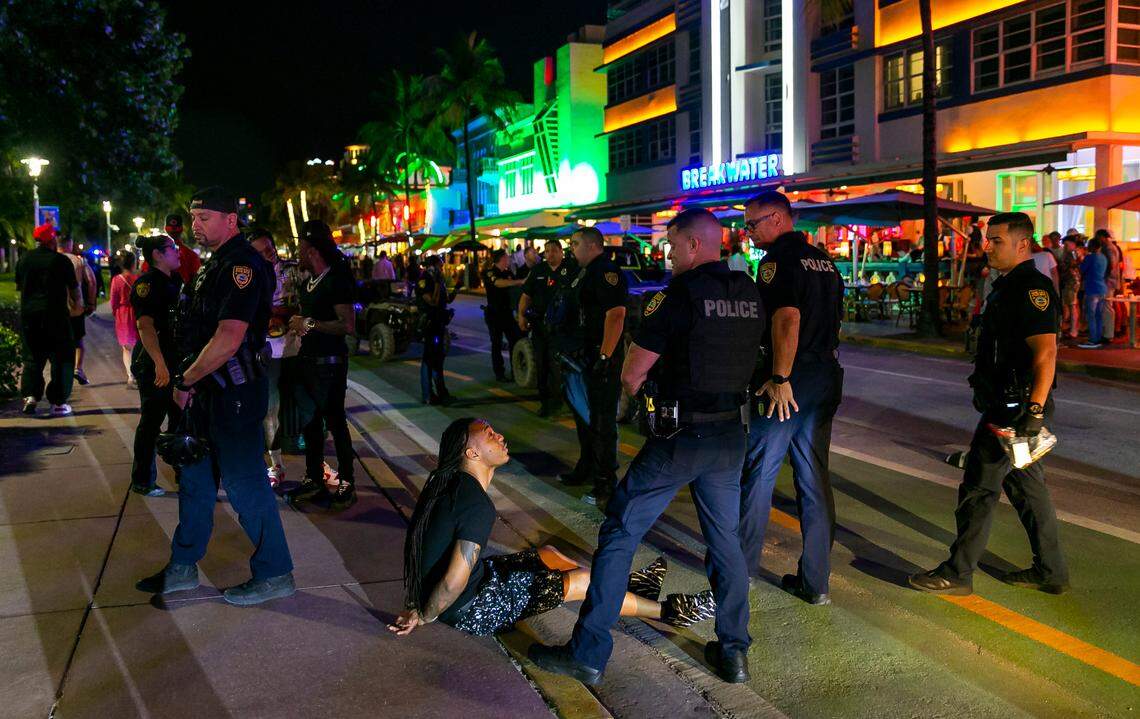 A man is detained by Miami Beach Police officers near Ocean Drive and 10th Street near Hotel Breakwater in Miami Beach, Florida, on Friday, March 25, 2022. City officials imposed a midnight curfew and forced stores to stop selling alcohol after 6 p.m. The restrictions were set in place after two shootings in Miami Beach the weekend before caused city officials to announce a “state of emergency.”