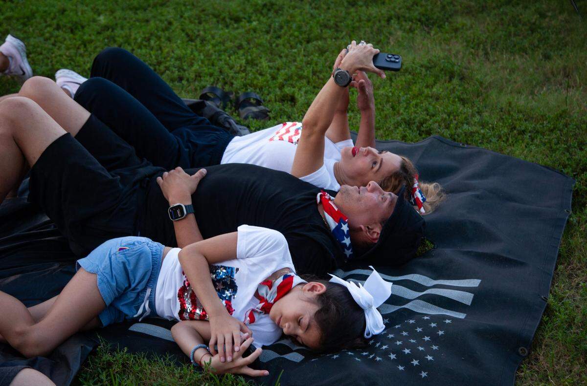 Fabiola Angulo, 46, looks at Instagram with her husband, Marlon Amaya, 49, and daughter, Marcella Amaya, 9, while waiting for the fireworks to start during the Fourth of July Bayfront Park Celebration at Bayfront Park on Tuesday, July 4, 2023 in Miami, Fla.