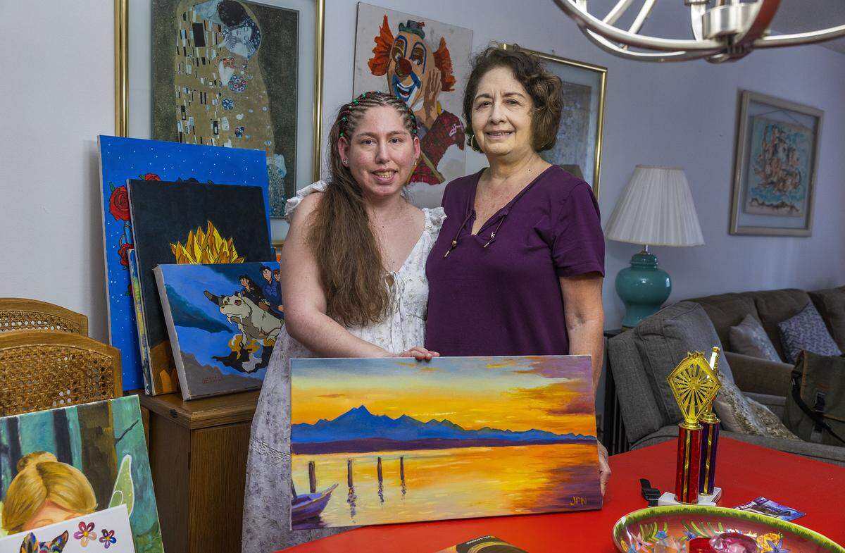 Rita Acosta and her daughter Jessica Novoa, posed with one of her paintings. Jessica is in her 40s and suffers from epilepsy since she was a little girl and a brain surgery some time ago as she continues to battle epilepsy. At her house, in Sunrise, Florida, on Saturday, December 13, 2025.