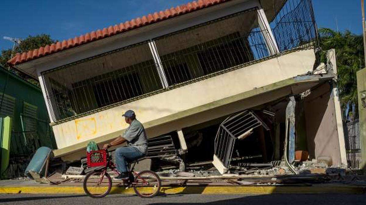 A man rides his bicycle past a house that has collapsed in Guanica, Puerto Rico, on Jan. 15, after a powerful earthquake hit the island.