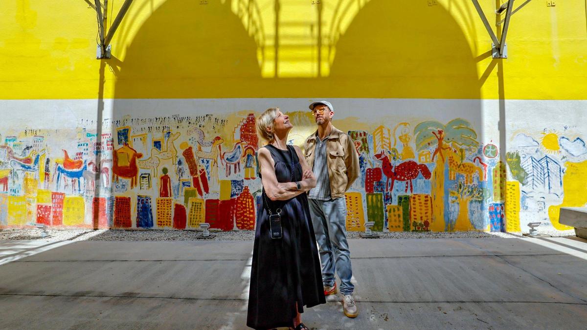 Bakehouse Art Center director Cathy Leff and artist Philip Lique, its technology strategist and planner, stand at the main entrance to the Wynwood complex, a former industrial bakery from 1926, in front of a mural by late Miami artist Purvis Young. Shadows on the mural are cast by a pair of surviving flour silos.