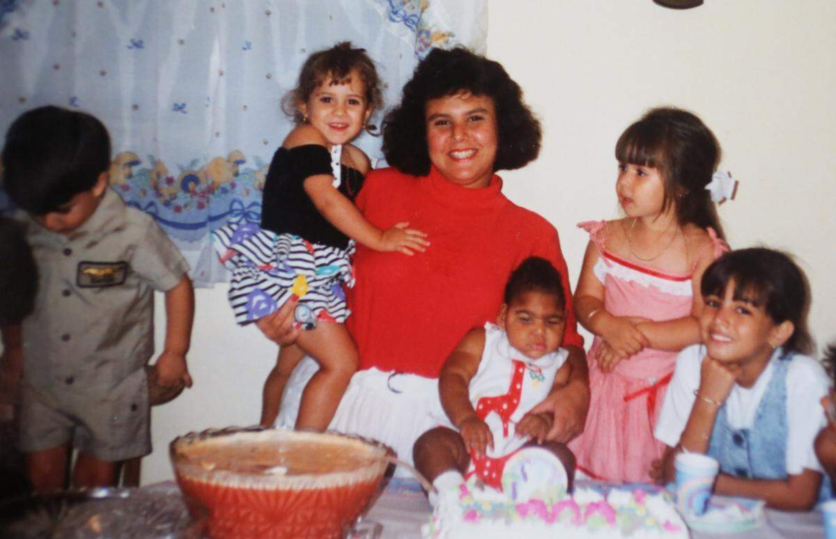 Jamie Acebo sostiene a la hija de un amigo en un brazo y mantiene a su hija pequeña, Jasmine, firme sobre la mesa durante la celebración del cumpleaños de Jasmine.