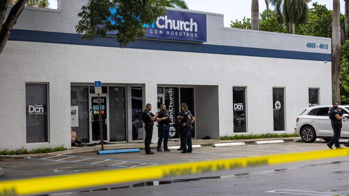 Doral police officers wait as a detained man sits in front of DCN Church off 4005 Northwest 79th Avenue after a shooting on Friday, July 5, 2024, near Doral, Fla. Three people were shot and one died, police said.