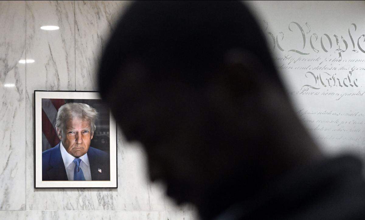Migrants line up in the lobby of the Jacob K. Javits Federal Building in New York near a wall bearing a portrait of President Donald Trump and the preamble to the U.S. Constitution. ICE agents and federal officers detain migrants after they attend immigration court hearings in the building amid a mass deportation effort in New York, Aug. 5, 2025. 
