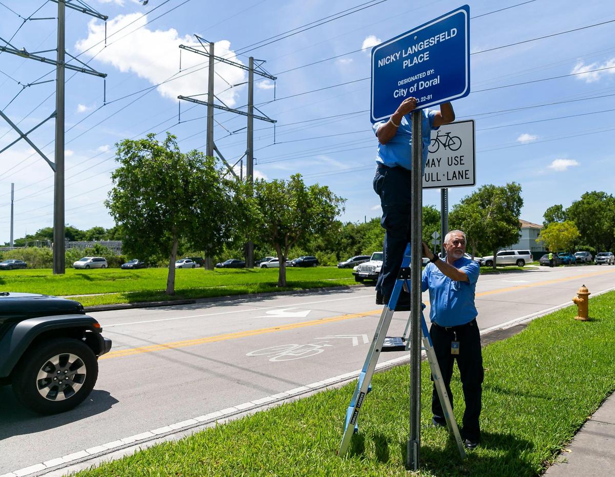 City of Doral employees Noel Suarez, center, and Orelvis Beltran, far right, help install a sign during a ceremony in honor of the late Nicole “Nicky” Langesfeld on Wednesday, June 22, 2022 in Doral, Florida.