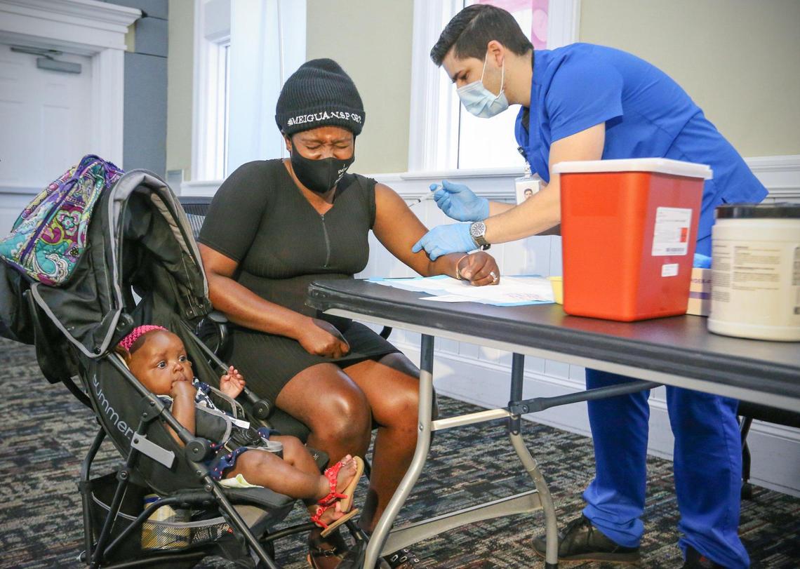 La residente de Chapman Partnership, Mirlange Jeune, es vacunada por el asistente médico Mauricio García mientras la hija de Jeune, Angela Exantus, observa. Las vacunas Moderna COVID-19 se administraron a los residentes, el personal y las familias en el refugio para personas sin hogar el 22 de abril.