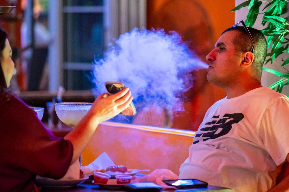 A man blows out hookah smoke at the outdoor patio of the Edison Hotel on Ocean Drive on Dec. 1, 2022. Because the patio area is on private property and not on the public sidewalk, the hotel can work around a city ban on hookah at sidewalk cafes.