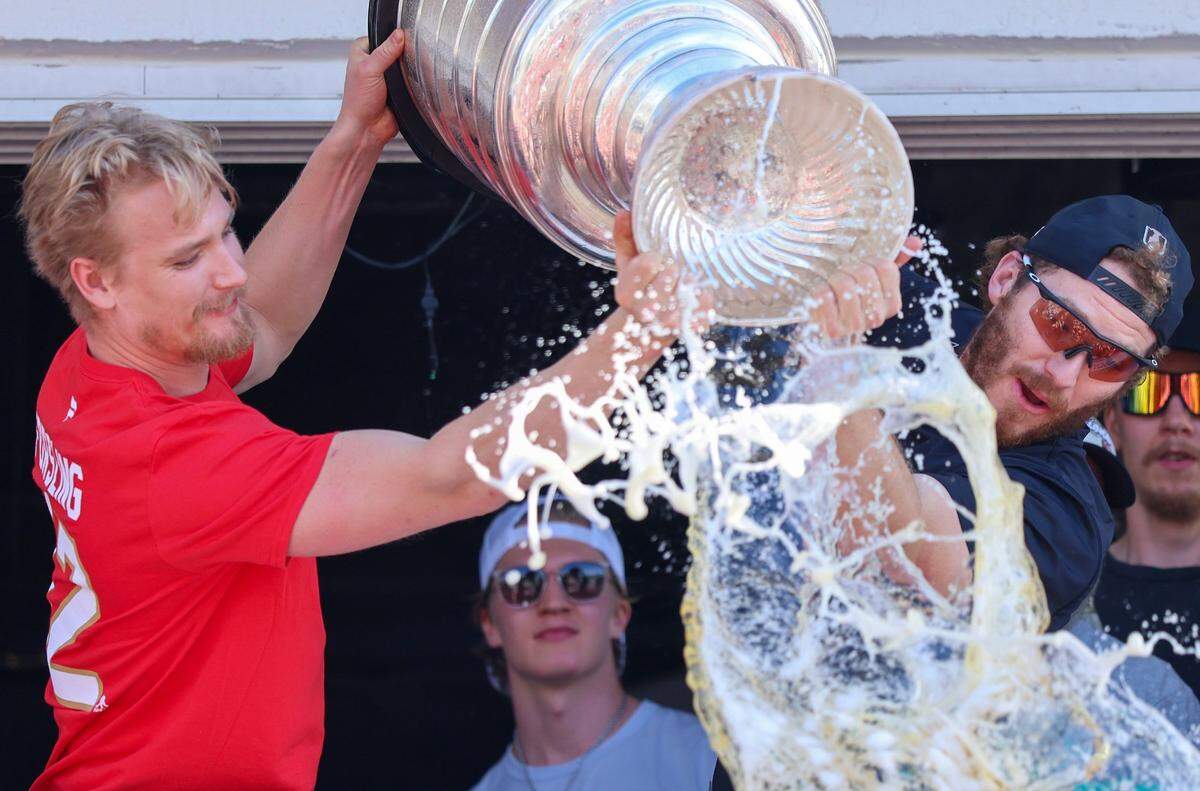 Gustav Forsling and Matthew Tkachuck pour beer from the Stanley Cup into the crowd below them at the Elbo Room while Anton Lundell looks on.