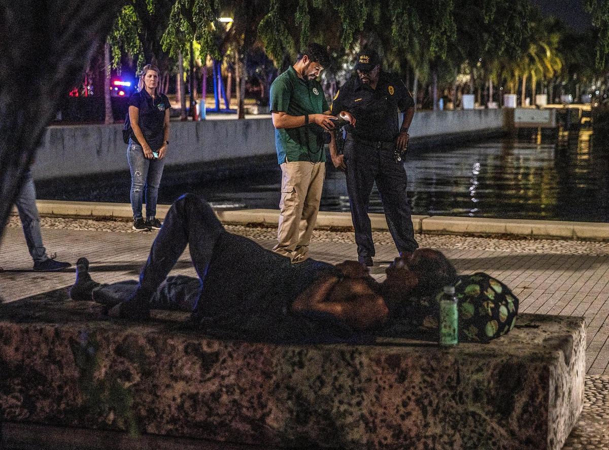 A homeless man sleeps on a bench at Museum Park as City of Miami Outreach Specialists Christian Candelier, left, and Ricky Leath, walked around the park during the annual Point-in-Time (PIT) Homeless summer census.