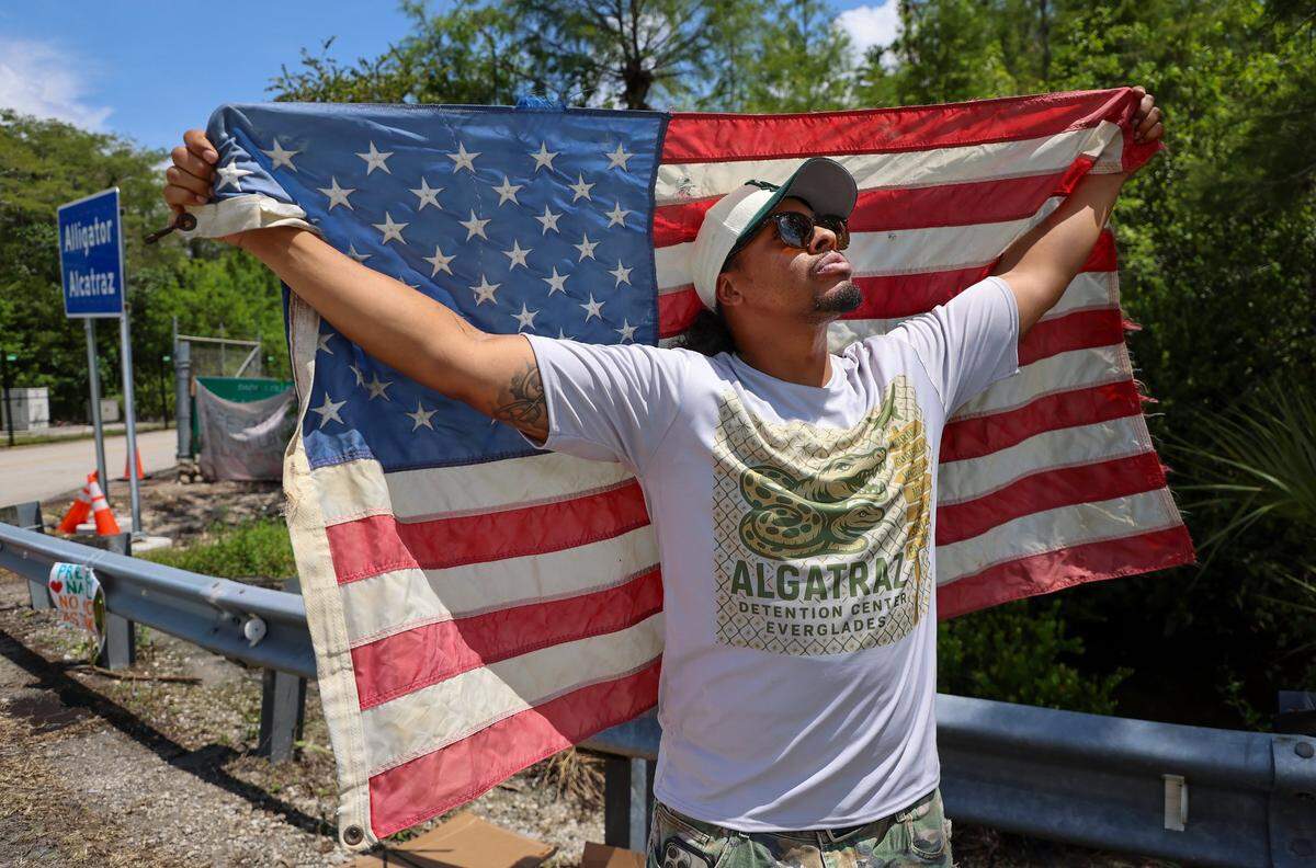 Michigan resident Chris Barrera, Sr., was seen stretching an aged American flag across his back at the entrance of the Dade-Collier Training and Transition Airport, also known as “Alligator Alcatraz.” He stood alongside a friend to show support for the newly constructed detention center located at the Collier and Miami-Dade county line on Sunday, July 6, 2025.
