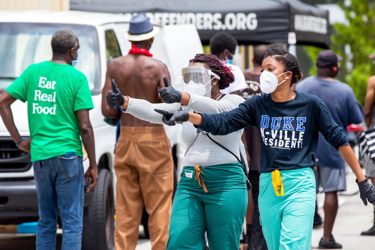 Two volunteer medical students assist in keeping the homeless six feet apart from one another as they wait for essential items being handed out during an event hosted by The Dream Defenders, in order to aid the unhoused at St. John Institutional Missionary Baptist Church in Overtown, Florida on Friday, April 24, 2020.