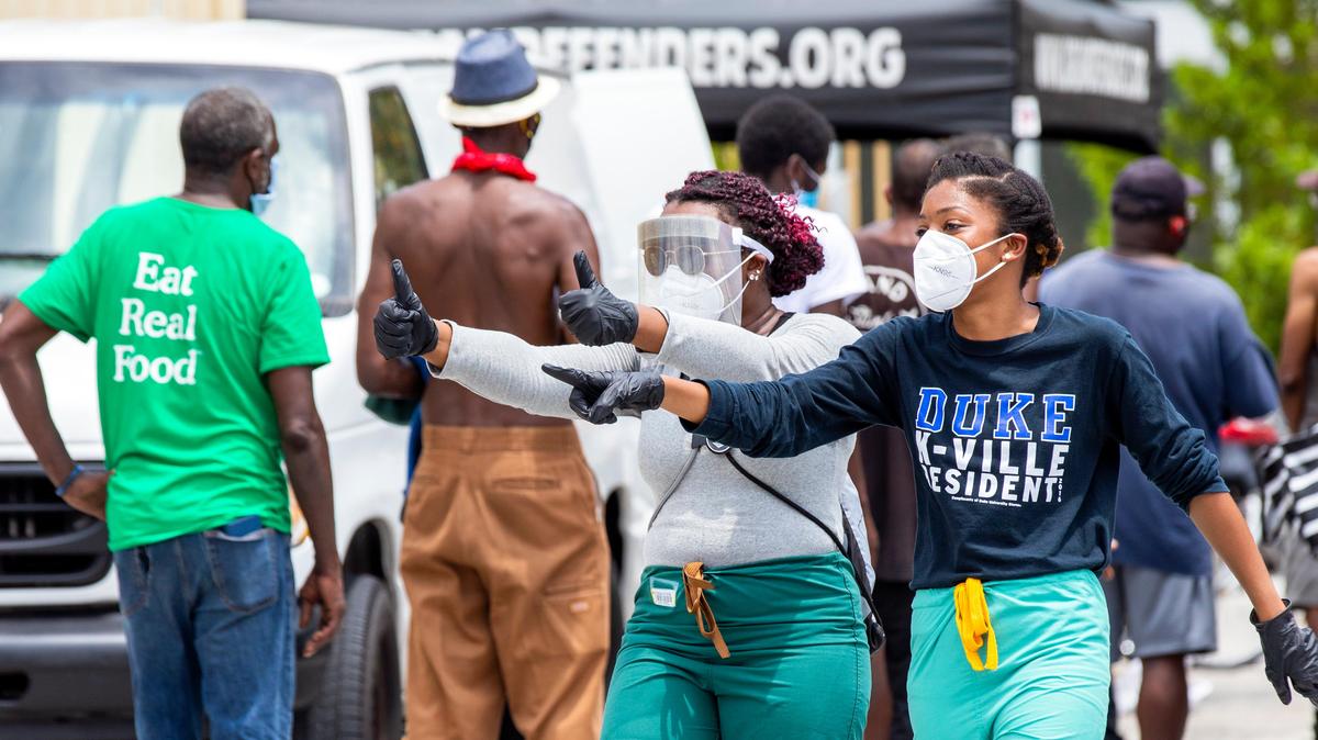 Two volunteer medical students assist in keeping the homeless six feet apart from one another as they wait for essential items being handed out during an event hosted by The Dream Defenders, in order to aid the unhoused at St. John Institutional Missionary Baptist Church in Overtown, Florida on Friday, April 24, 2020.