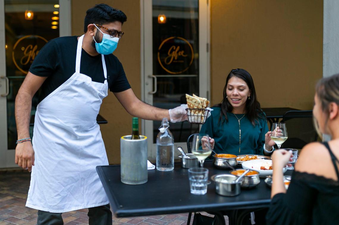 Niven Patel, the owner of Ghee Indian Kitchen, serves guests food at his restaurant in Dadeland. Patel puts on gloves to run food to a table then discards them.