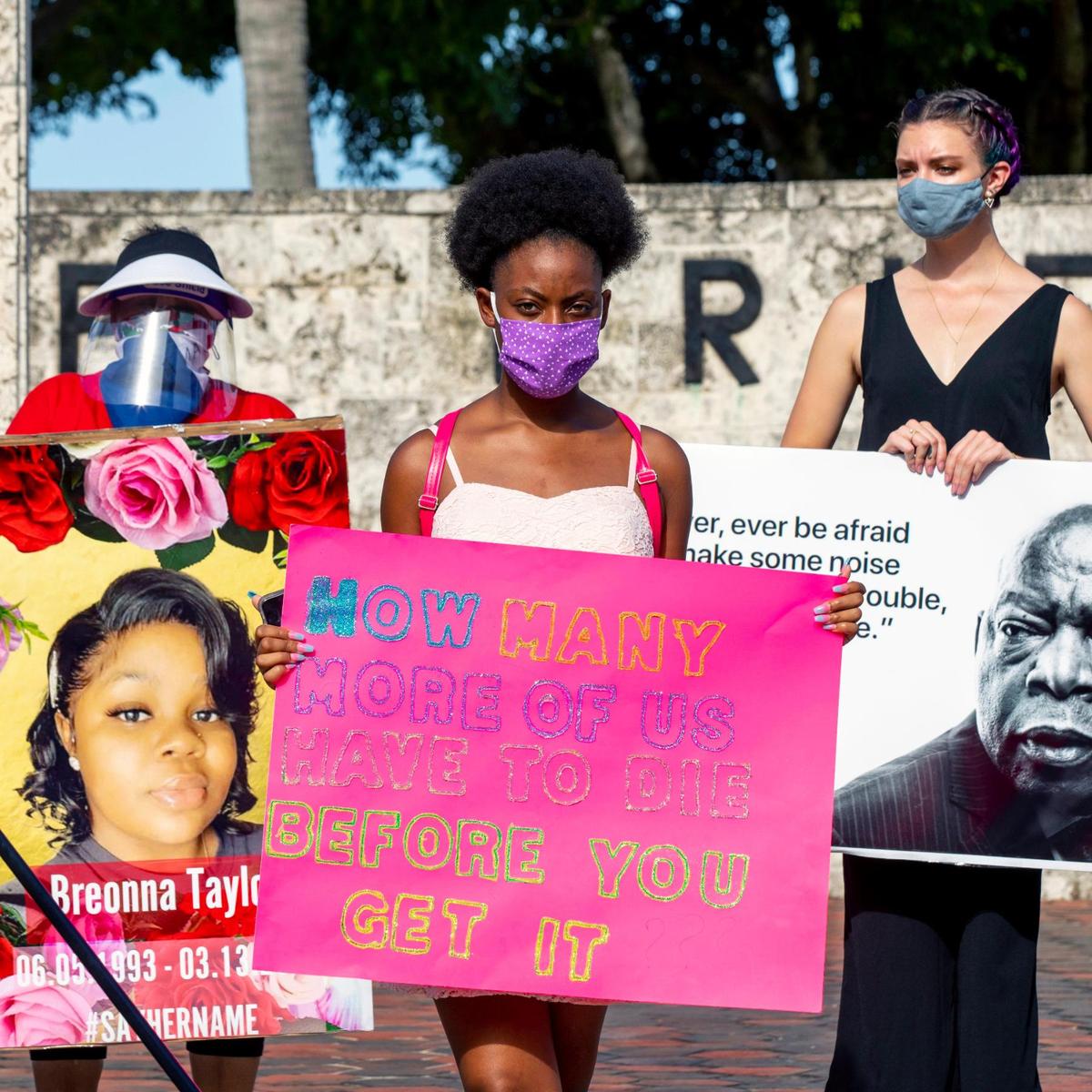Activist Yasmin Webb and others hold signs while speakers share their experiences of getting arrested during a Black Lives Matter protest to denounce what they say is excessive force by police in confronting the protesters. The rally of about 40 people took place at The Torch of Friendship in Miami on Tuesday, July 28, 2020.