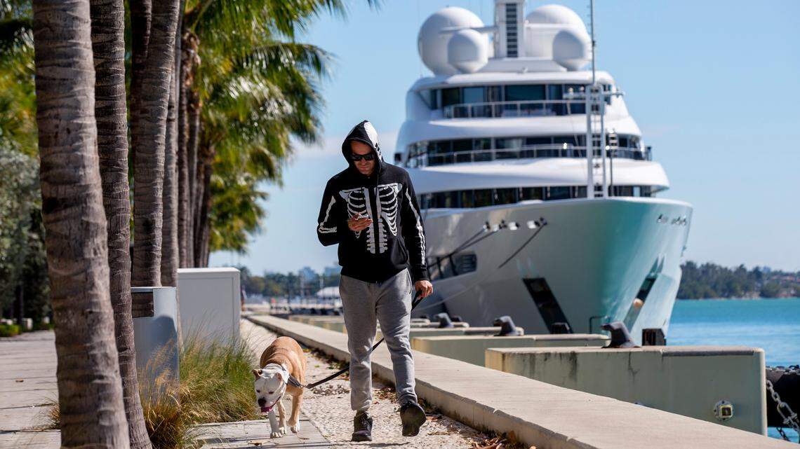 David Gutierrez, 39, walks his dog in the cold weather at Maurice A. Ferré Park as a yacht named Naia sits in the background in Miami, Florida, on Jan. 22, 2020.