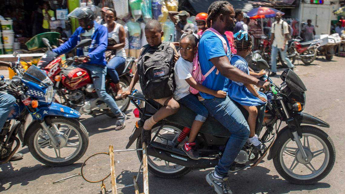 A man driving a motorcycle transporting children breaks through a barricade set up by medical students demanding the release of a professor who was kidnapped last week, in Port-au-Prince, Haiti, Friday, April 30, 2021. Catholic officials rejoiced on Friday after kidnappers in Haiti released nine people, including five priests and two nuns.