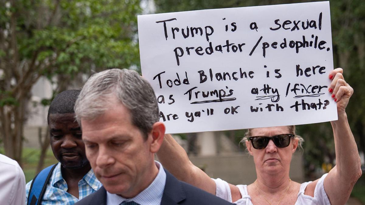 A protester holds a sign behind Ghislaine Maxwell’s Miami defense attorney David O. Markus outside the federal courthouse in Tallahassee, Florida, on Friday, July 25, 2025. Markus is representing Maxwell, who is serving a 20-year prison sentence in Tallahassee after being convicted for recruiting underage girls to engage in illegal sex acts with Jeffrey Epstein. Maxwell was deposed on Thursday and Friday by Todd Blanche, a top Justice Department official.