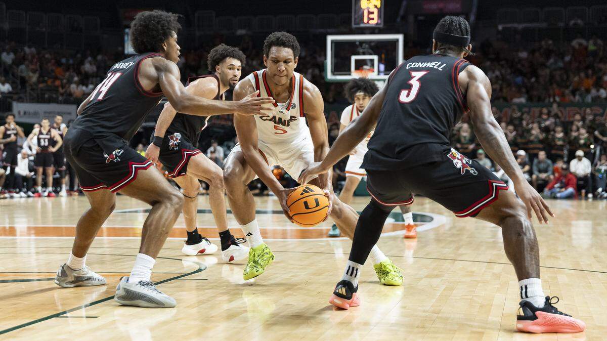 Miami Hurricanes forward Malik Reneau (5) drives the ball as Louisville Cardinals guard Adrian Wooley (14) and guard Ryan Conwell (3) defend in the second half of their NCAA basketball game at the Watsco Center on Saturday, March 7, 2026, in Coral Gables, Fla.