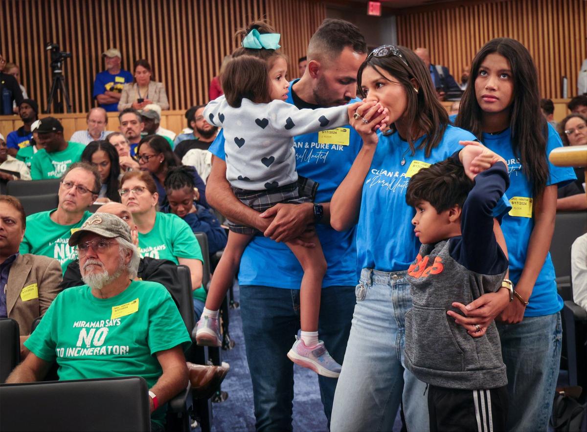 Edwin Vale, 35, carries his 4-year-old daughter, as his wife Ana Vale, 34, center, kisses her daughter’s hand while standing with their 15-year-old and 7-year-old son, prior to giving comments opposing the incinerator returning to Doral on Tuesday, Sept. 17, 2024, at Miami-Dade Commission meeting in Miami.