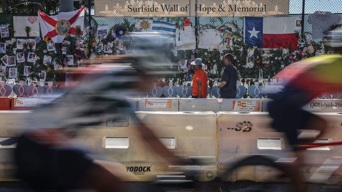Cyclists ride past the Wall of Hope and Memorial in Surfside on Sunday, July 18.