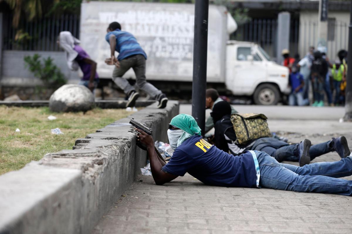Armed off-duty police officers take cover during an exchange of gunfire with army soldiers during a protest over police pay and working conditions, in Port-au-Prince, Haiti, Sunday, Feb. 23, 2020.