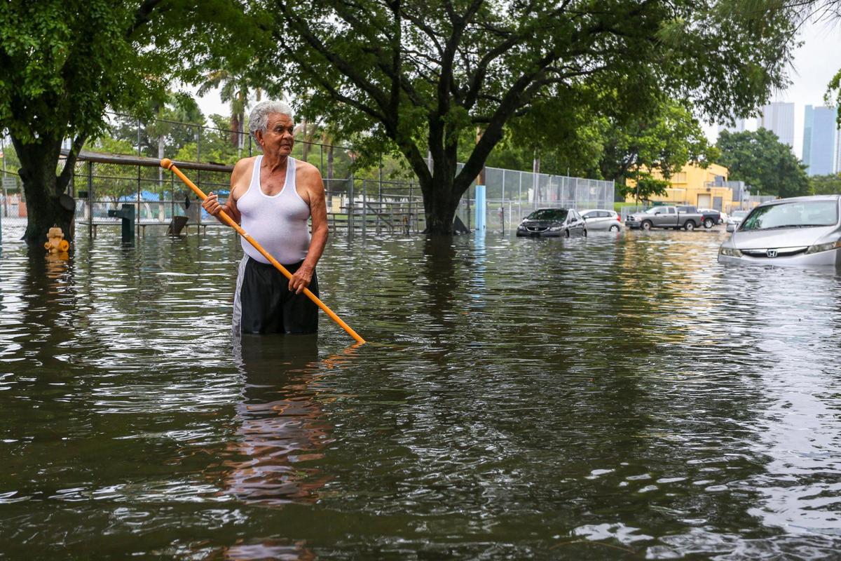 Mario Leiva, 75, uses a stick in an attempt to unblock the sewer drainage on the corner of Southwest Eighth Avenue and Fourth Street in the neighborhood of Little Havana in Miami, Florida, on Saturday, June 4, 2022.