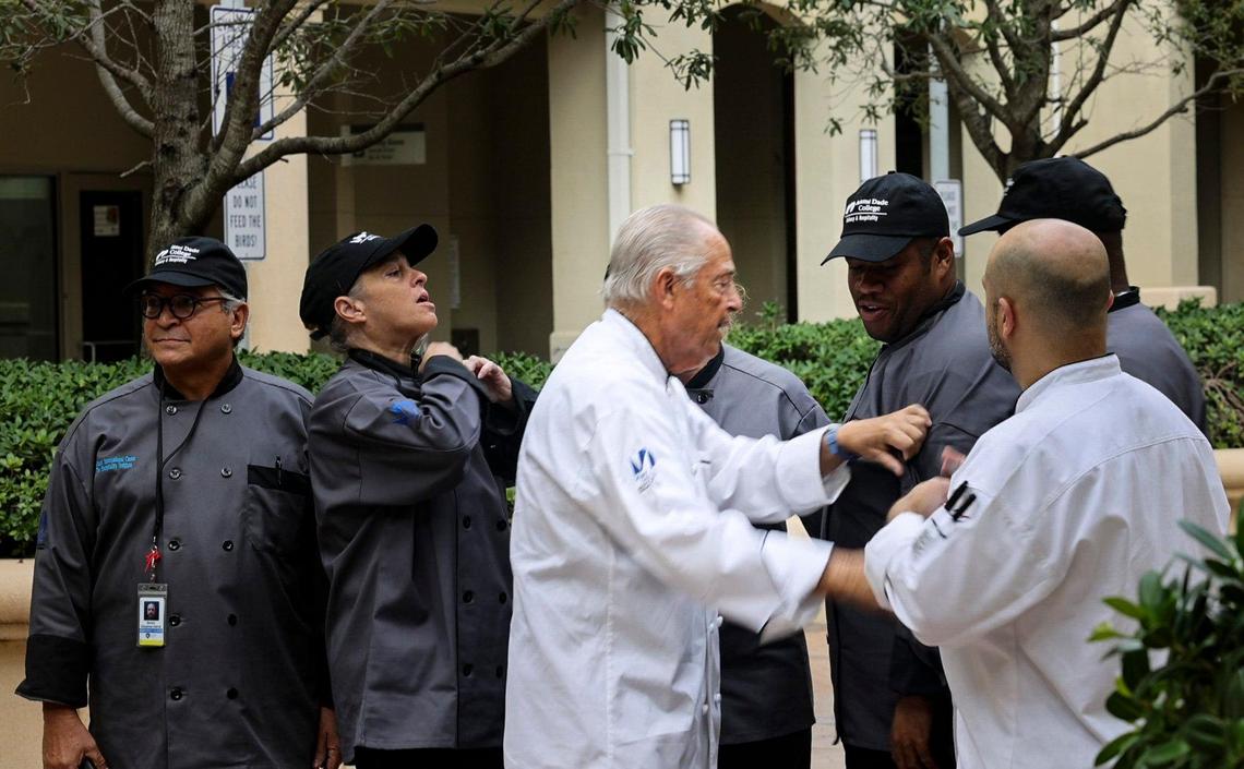 Frank Ferrara, center, culinary instructor and life skills coach, helps one of his students adjust their uniform after a press conference announcing a $2 million city donation to Camillus House as part of the “Functional Zero” homeless plan on Friday, Oct. 14, 2022, in Miami. Camillus House has programs on its campus in affiliation with Miami Dade College and Florida International University to give courses in construction and culinary arts to people trying to get off of the streets.