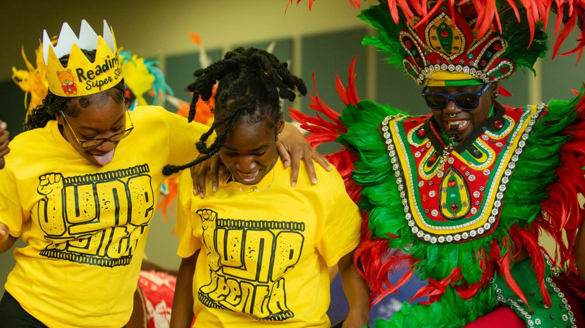 A member of a Bahamian Junkanoo band dances with summer camp counselors at the Overtown Optimist Club’s third annual Juneteenth event at Theodore Gibson Park gym on Wednesday, June 19, 2024 .