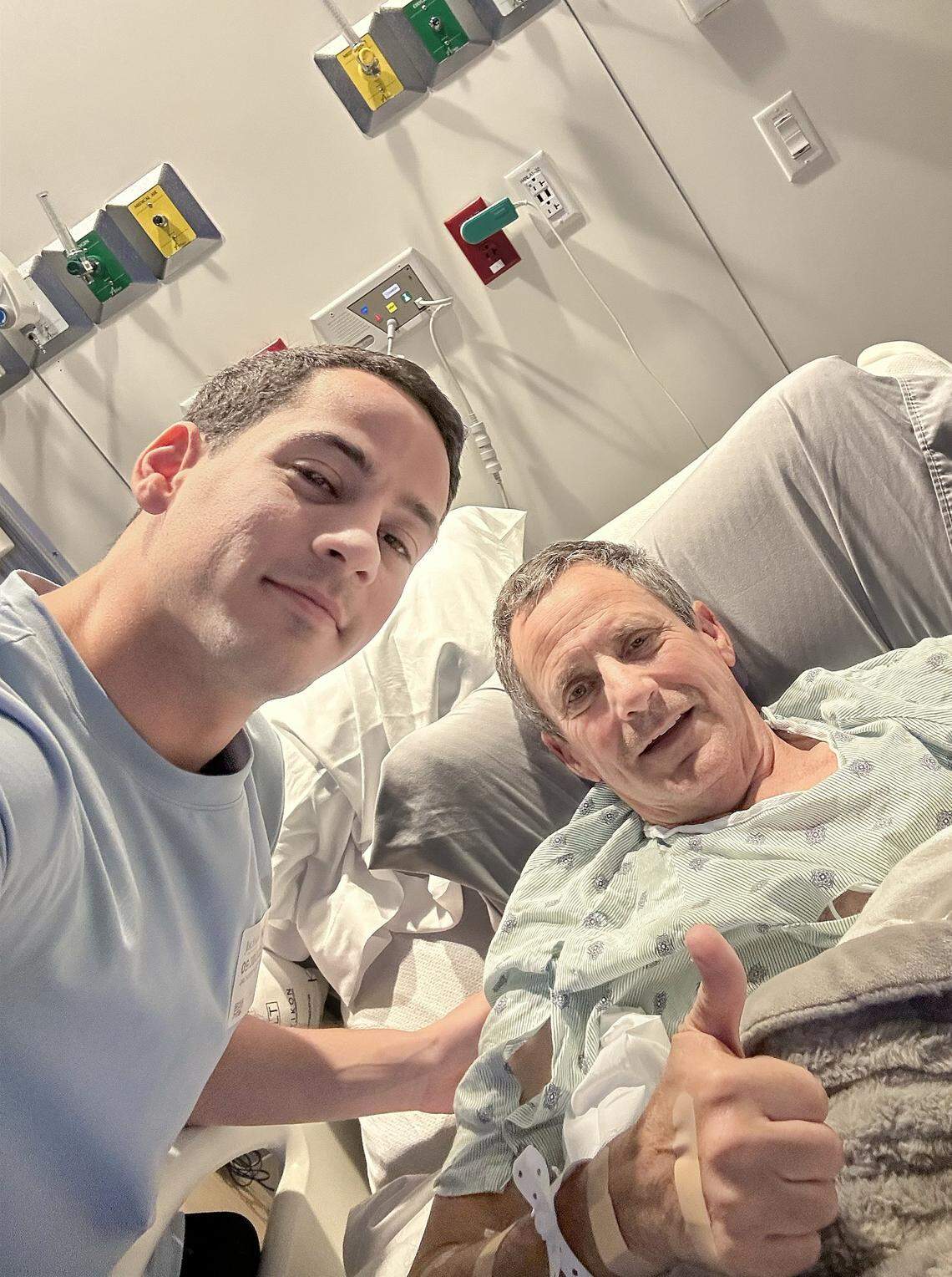 Pablo Langesfeld, right, who lost his daughter and son-in-law in the 2021 Champlain Towers collapse, gives a thumb-up with his son Martin Langesfeld, left, during a hospital visit. (Photo Courtesy of Martin Langesfeld) Langesfeld, now battling advanced pancreatic cancer, is suing Oscar Health Insurance for denying coverage of a drug therapy his doctors recommend, underscoring broader struggles over access to treatment.