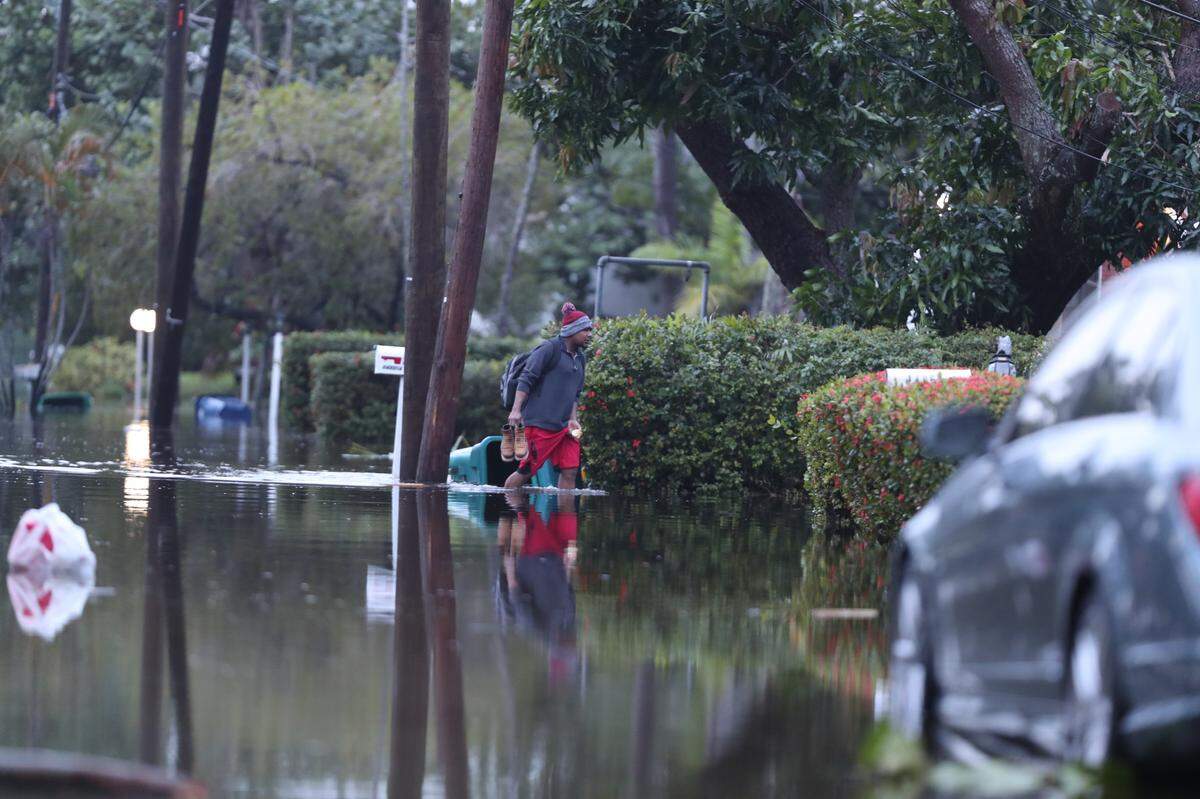 A man walks through flood waters while carrying his shoes in North Miami in the morning of Thursday, Nov. 16, 2023.