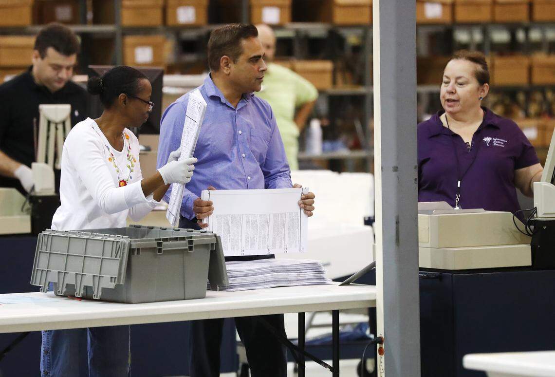 Employees at the Palm Beach County Supervisor of Elections office feed ballots through a machine Tuesday, Nov. 13, during the ongoing recount as they race to make a Thursday deadline.
